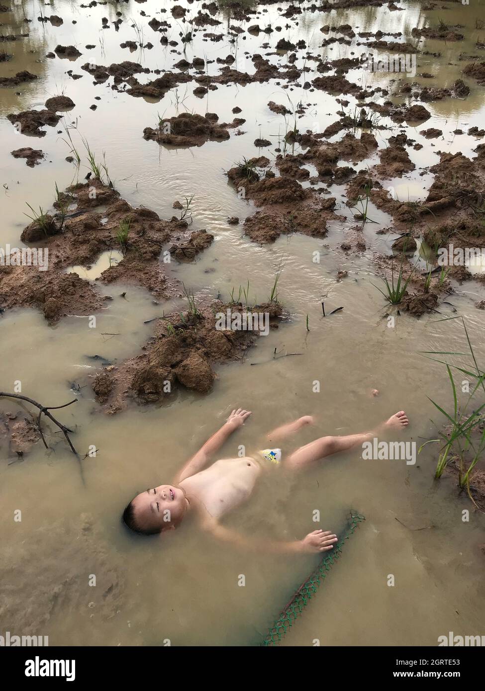 High Angle View Of Shirtless Boy Lying In Muddy Water Stock Photo