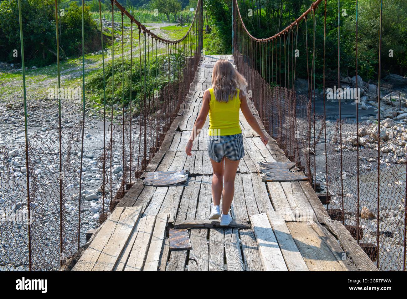 a girl in yellow walks along a suspension bridge  Stock Photo