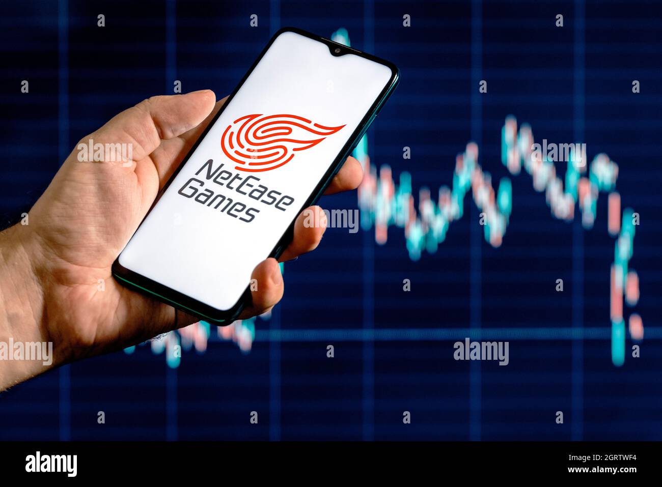 A smartphone with the NetEase logo in a hand. Stock chart on the background. Stock Photo