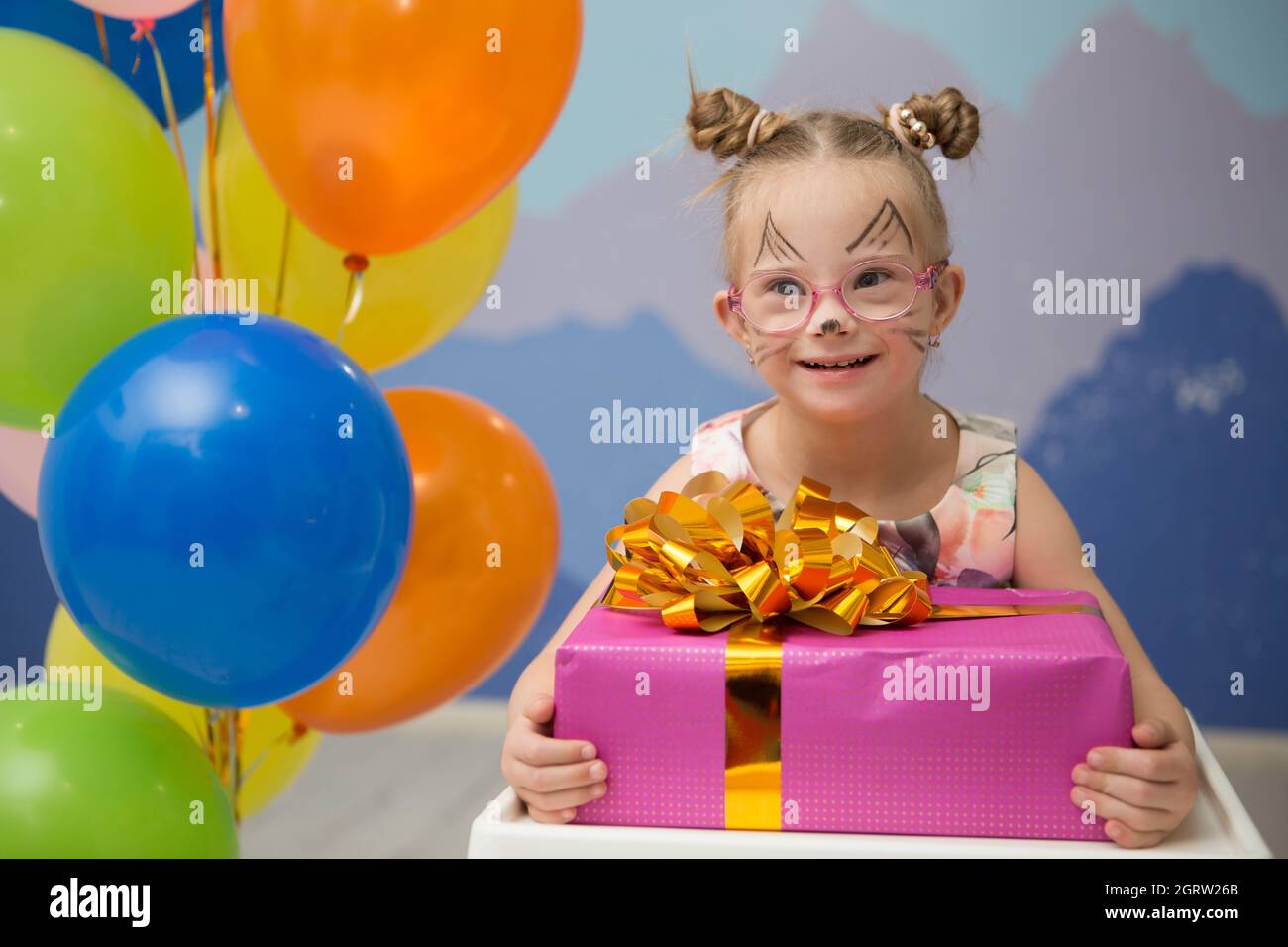 Beautiful girl with Down syndrome holds a big gift for her birthday Stock Photo