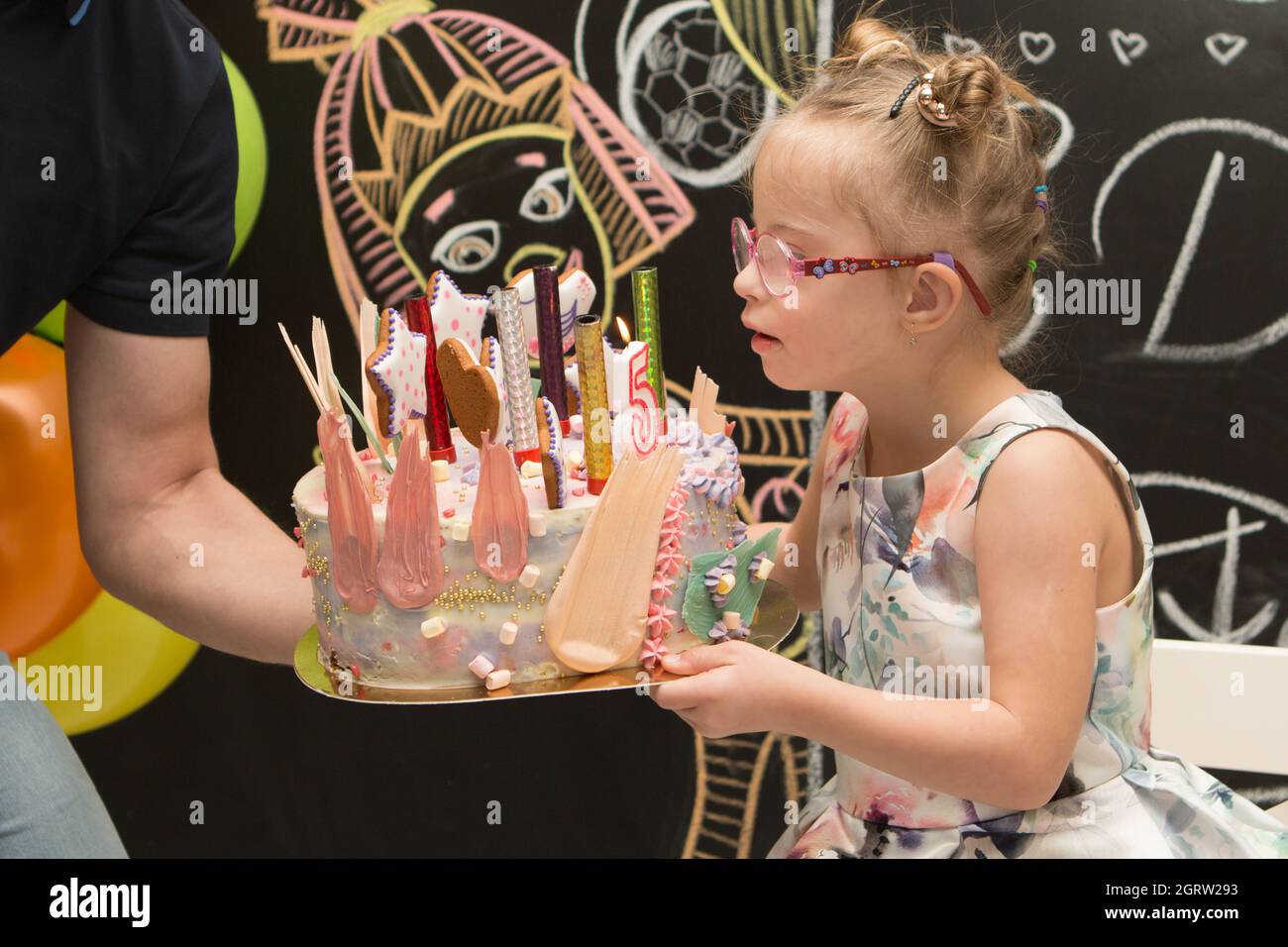 A girl with Down syndrome blows out candles on a cake on her birthday and make wishes Stock Photo