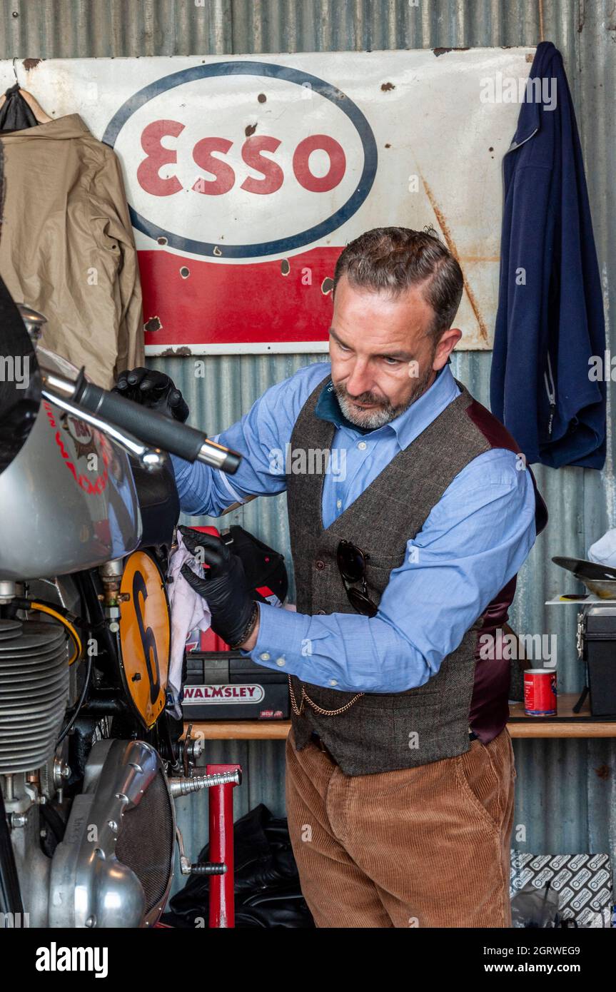 Vintage motorcycle receiving attention from a male in period attire in a classic garage scene at the Goodwood Revival. Classic Esso brand logo Stock Photo