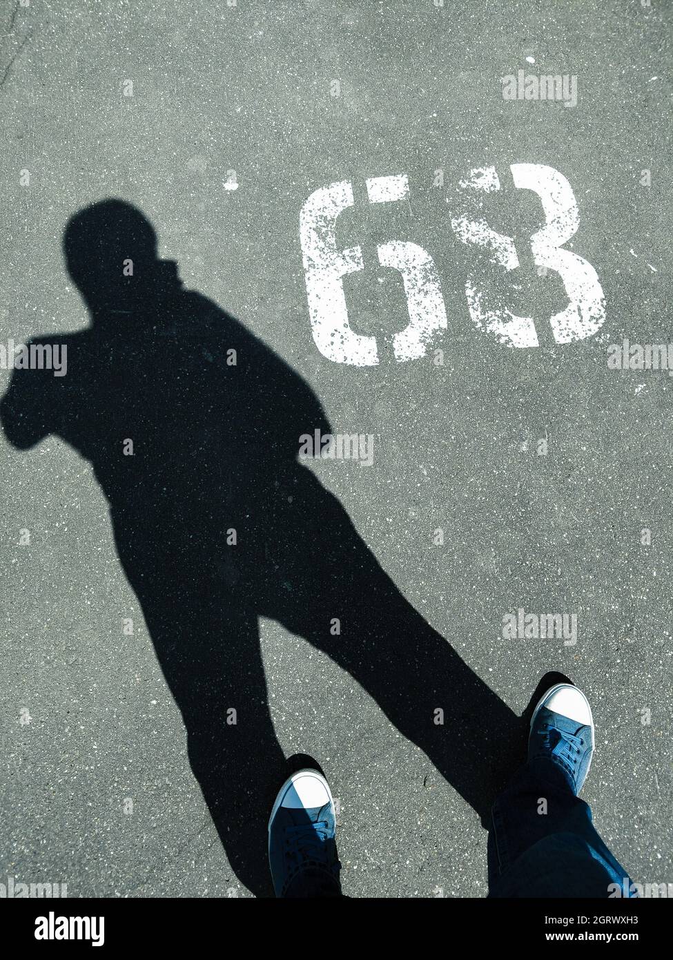 Low Section Of Man Wearing Shoes While Standing On Road With Number Stock Photo