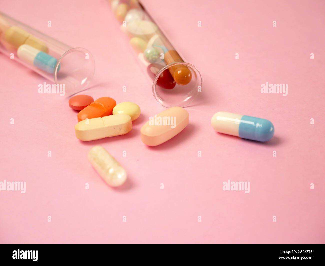 Medicines Spilling From Test Tubes Over Pink Background Stock Photo