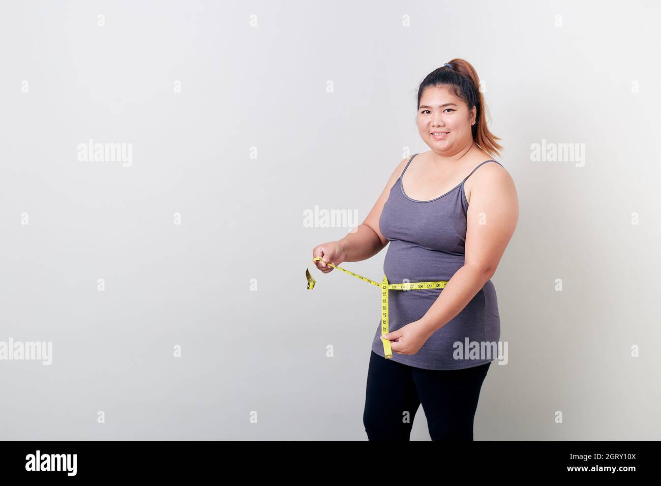Portrait Of Woman Measuring Waist Against White Background Stock Photo