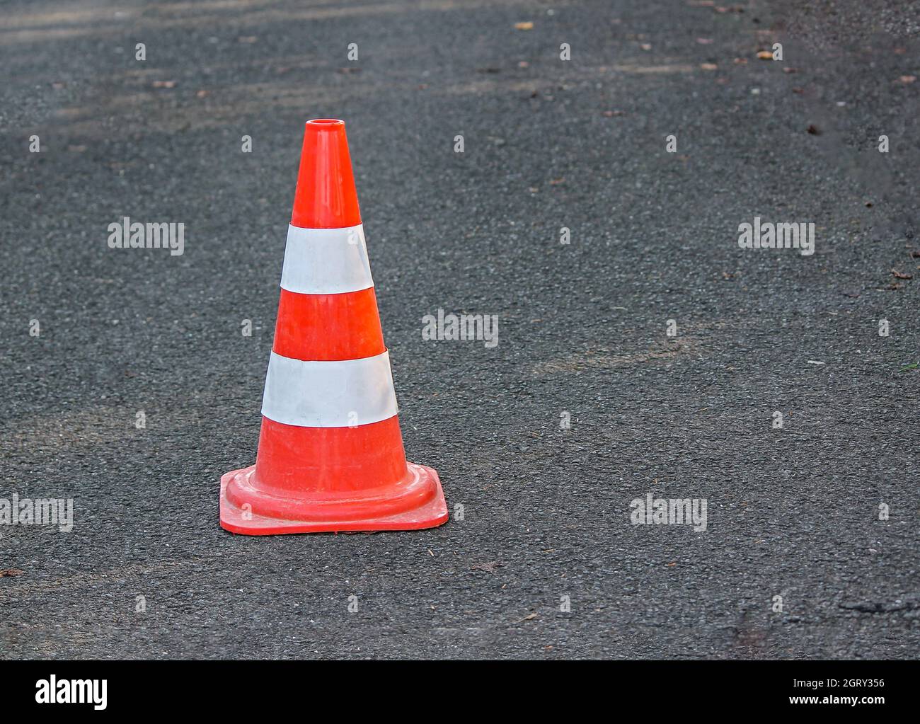 Orange road cone with white stripes stands on the roadway Stock Photo