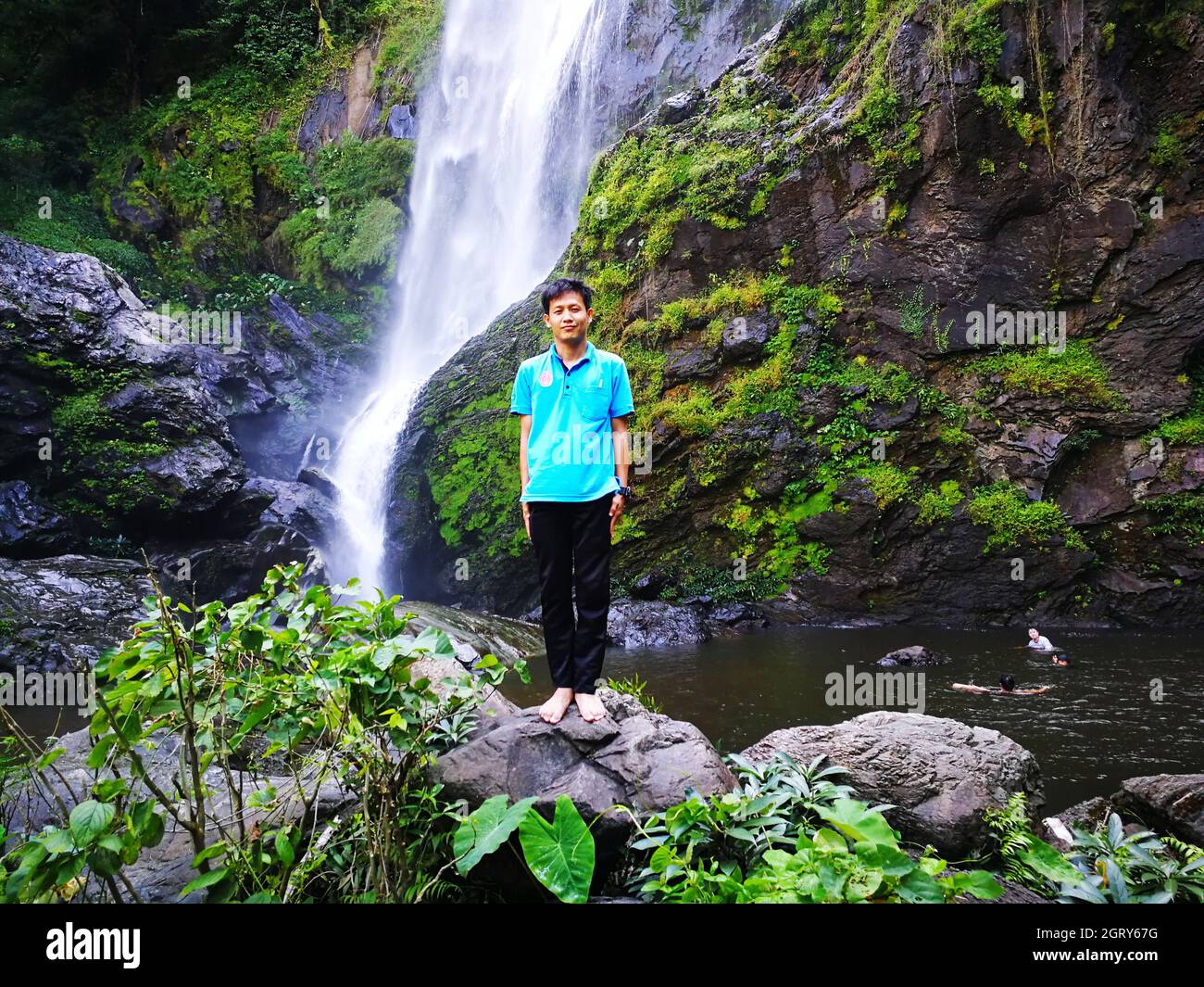 Low Angle View Of Mid Adult Man Standing On Rock Against Waterfall Stock Photo