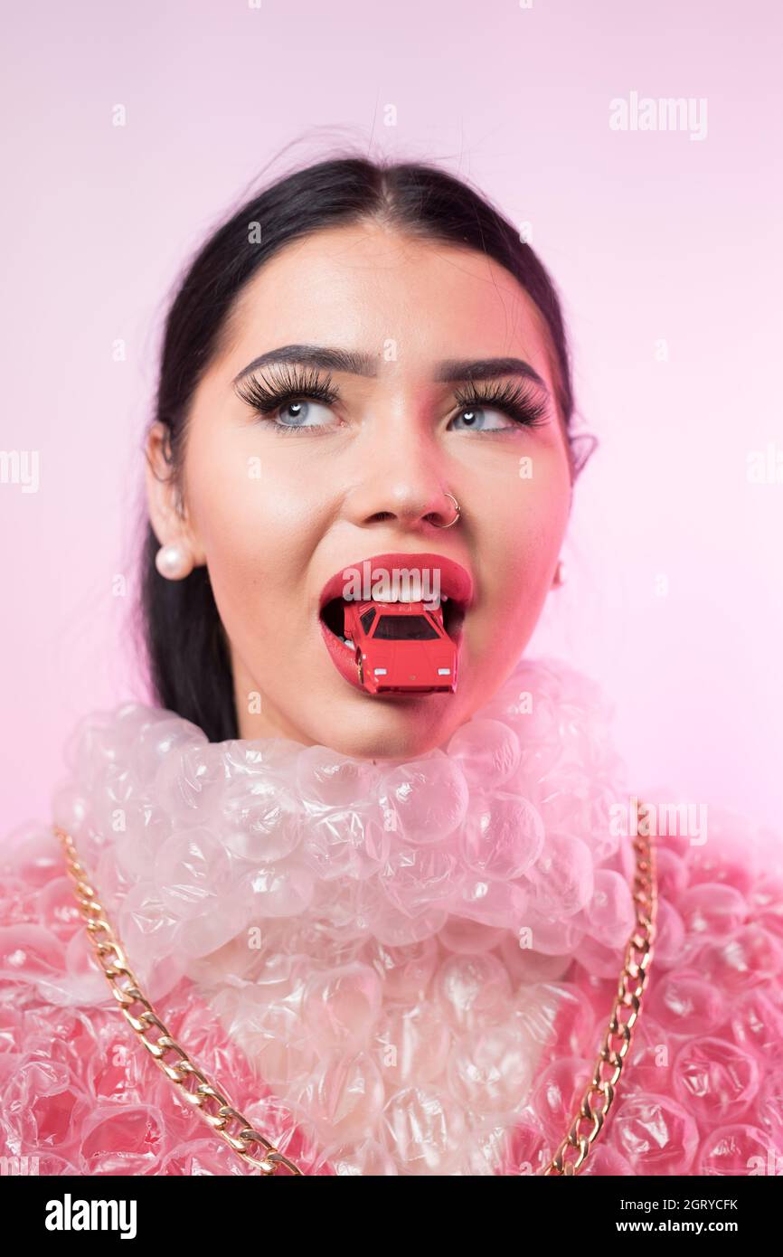 Young Woman Wearing Bubble Wrap With Toy Car In Mouth Against Pink