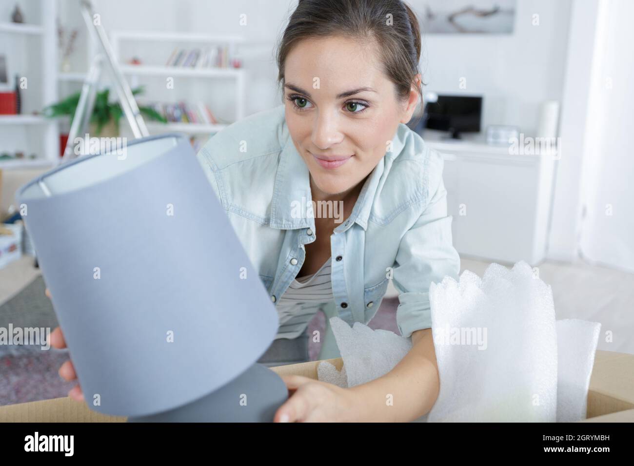 woman unpacking lamp from cardboard box in her new home Stock Photo