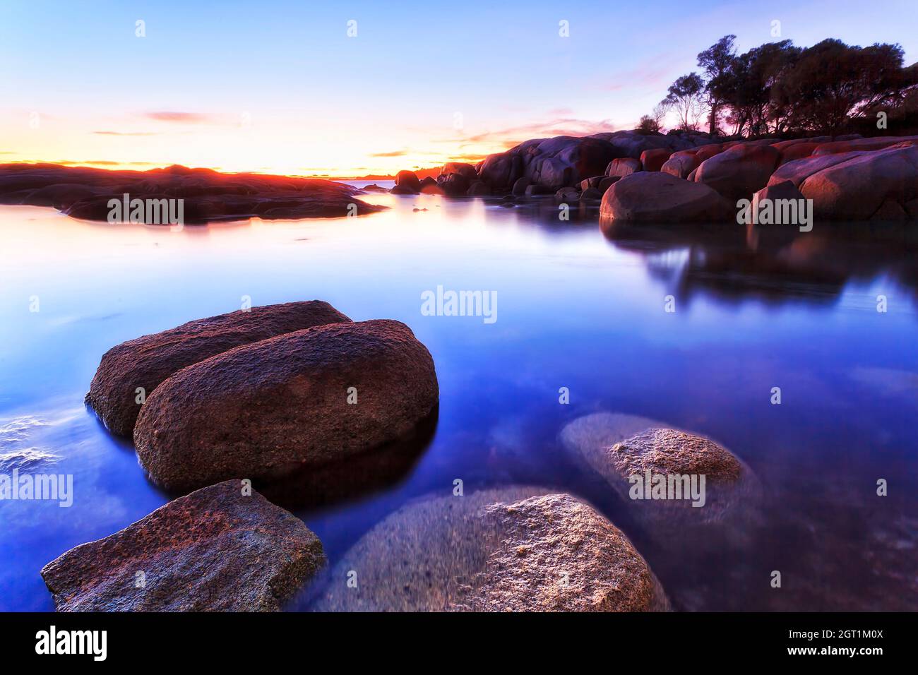 Dark dawn seascape of red lichen granite boulders in Binalong bay of Tasmania, AUstralia. Stock Photo