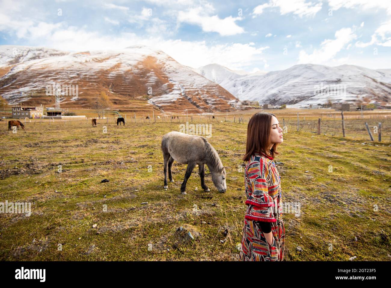 Side View Of Woman Standing On Field Against Snowcapped Mountains Stock Photo