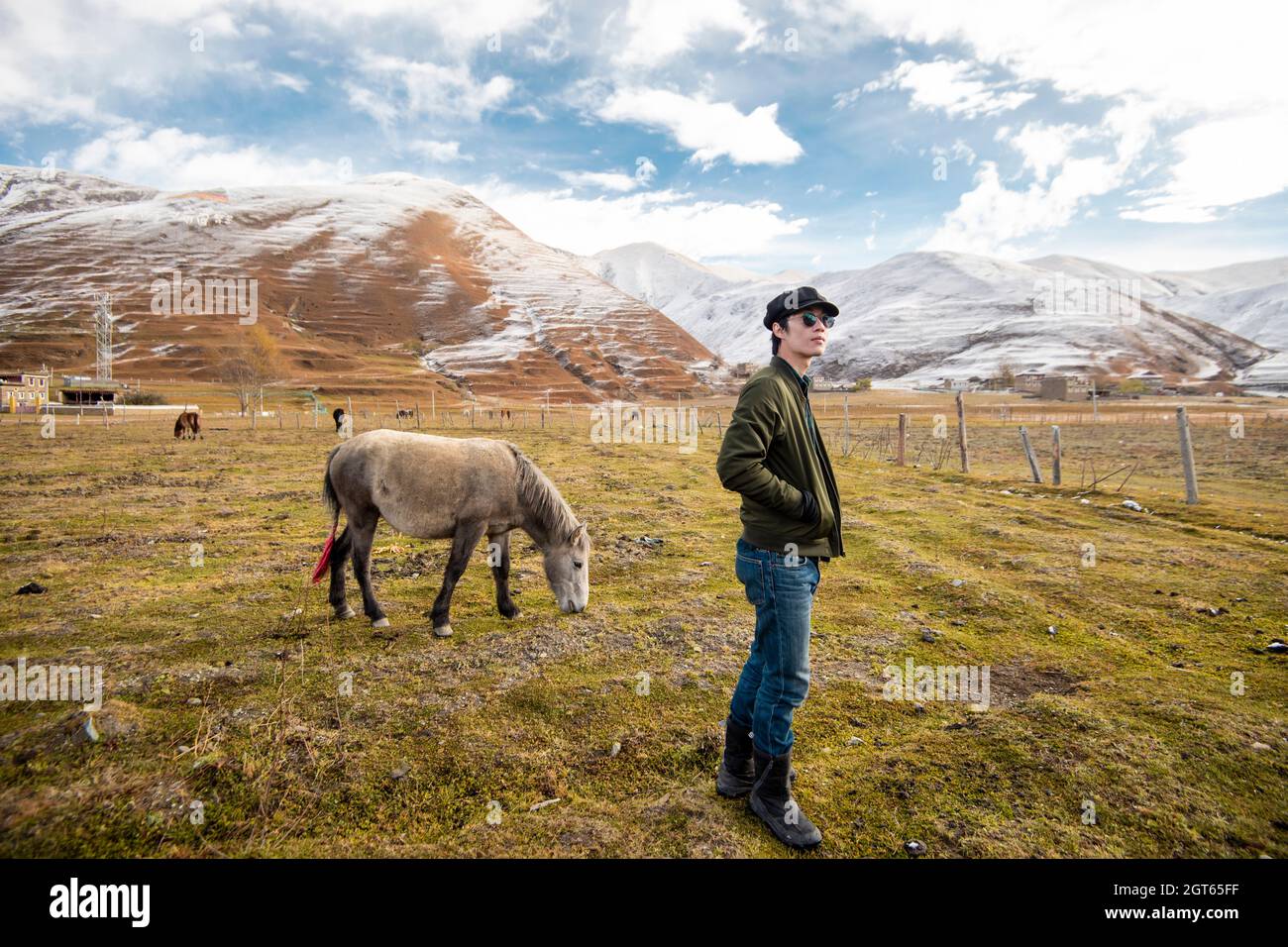 Side View Of Man Standing On Field Against Snowcapped Mountains Stock Photo