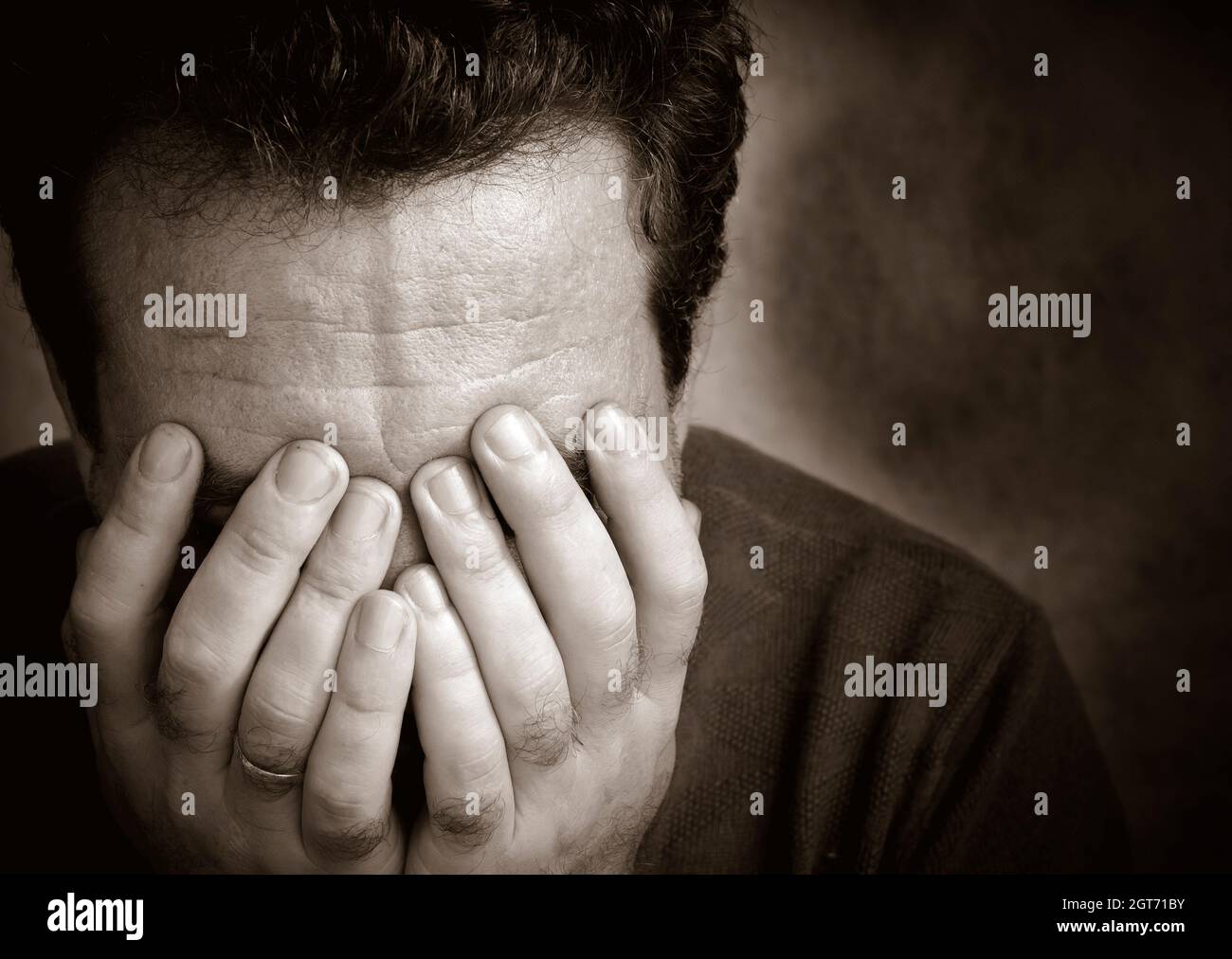 Close-up Of Man Covering Face Against Wall Stock Photo