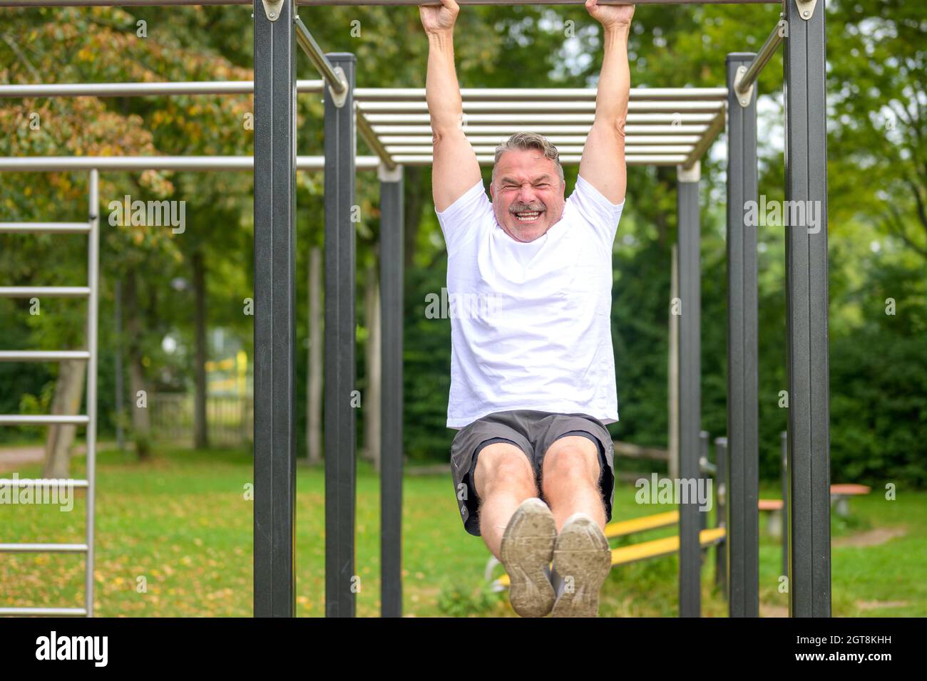 Senior man working out on parallel bars in a park in spring raising his