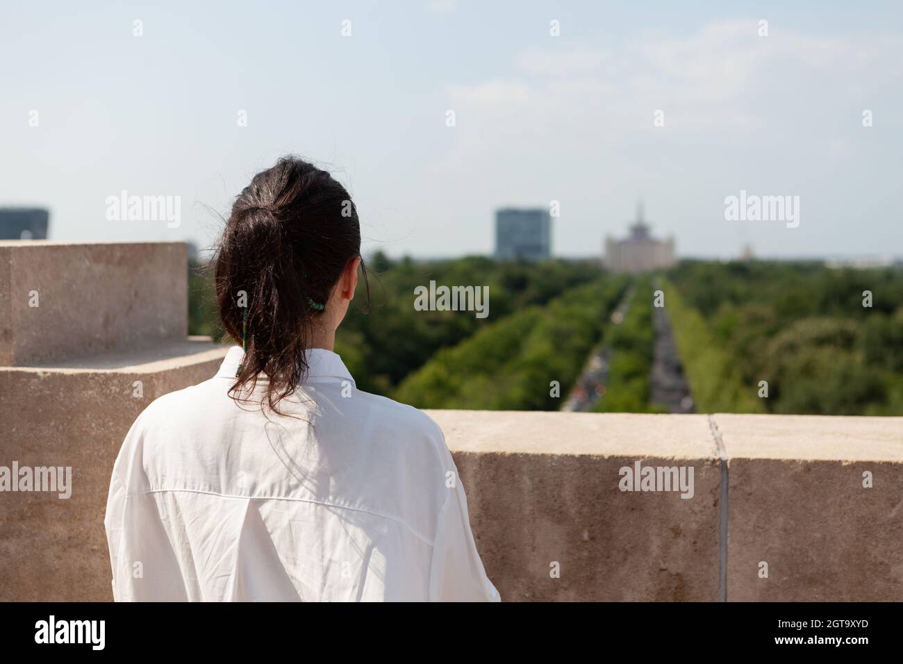 Woman toursit standing on building rooftop enjoying seeing panoramic view of metropolitan city during summer vacantion. Landscape with urban buildings from observation point Stock Photo