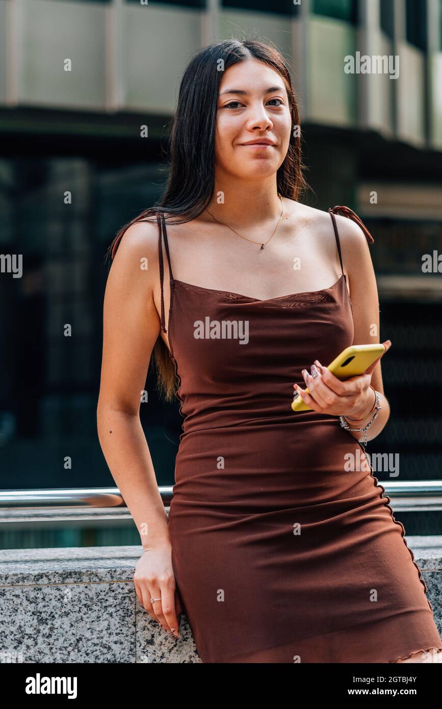 vertical portrait of an asian young woman holding a yellow phone. She is looking at camera and smiling Stock Photo