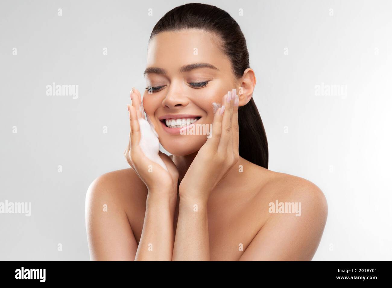 Happy girl with perfect glowing skin applying foaming cleanser for skincare and moisturizing at home Stock Photo
