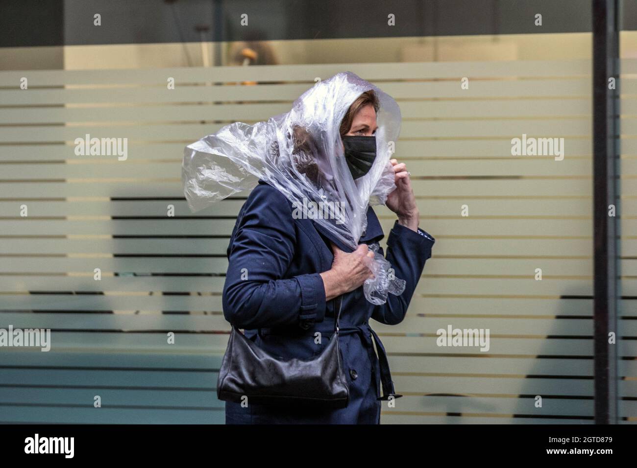 Keeping hair dry in Southport, Lancashire.  UK Weather. 02 Oct 2021. Strong winds and heavy showers in the town centre.    Credit: MediaWorldImages/AlamyLiveNews Stock Photo