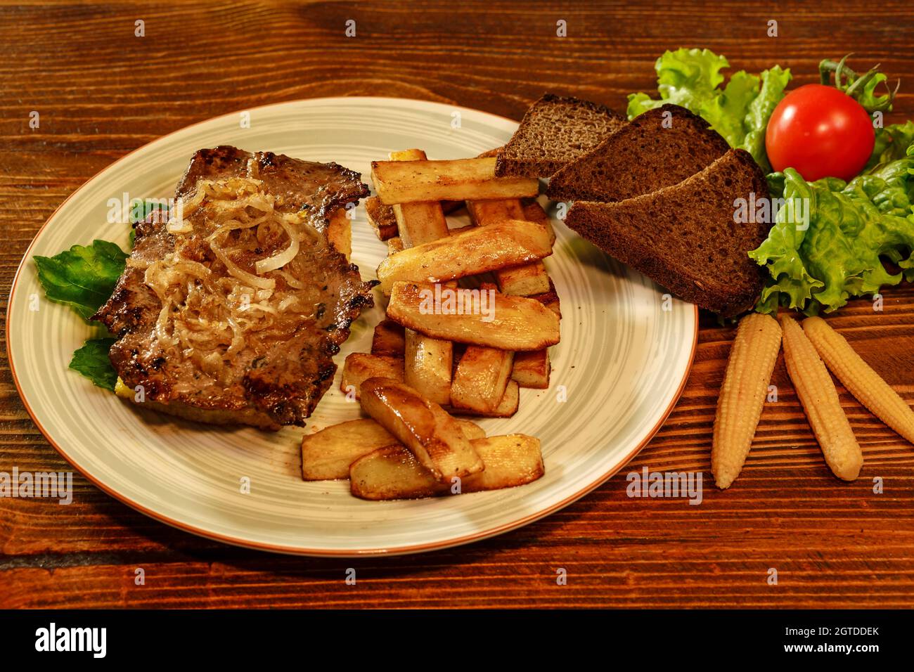 Tasty sheet pan steak with homemade crispy baked french fries decorated with black bread, cherry tomatoe and marinated baby corns. Restaurant food clo Stock Photo