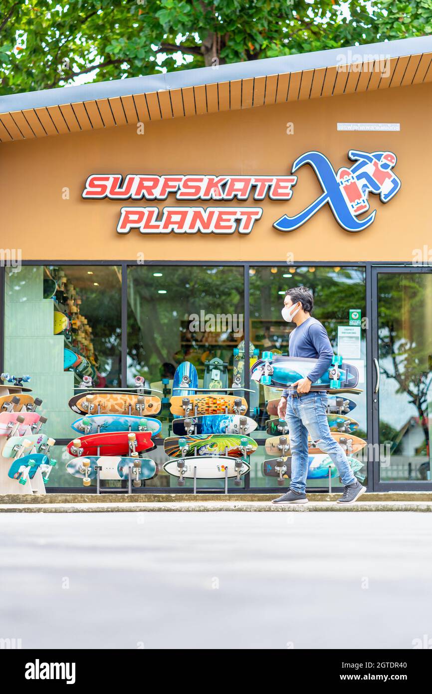 "Asian Cheerful man holding surfskate and walking in front of the