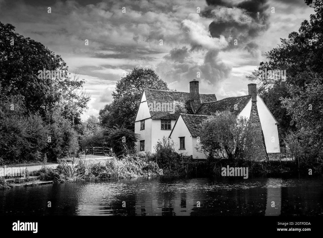 Black and white image of Willy Lotts cottage at Flatford Mill Suffolk UK made famous by John Constable. Dramatic clouds and still water. No people. Stock Photo