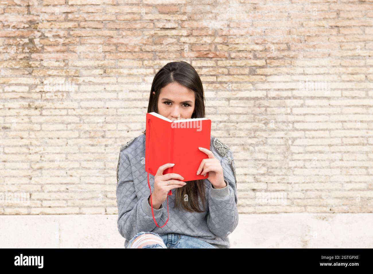 Portrait Of Woman Holding Book Against Brick Wall Stock Photo