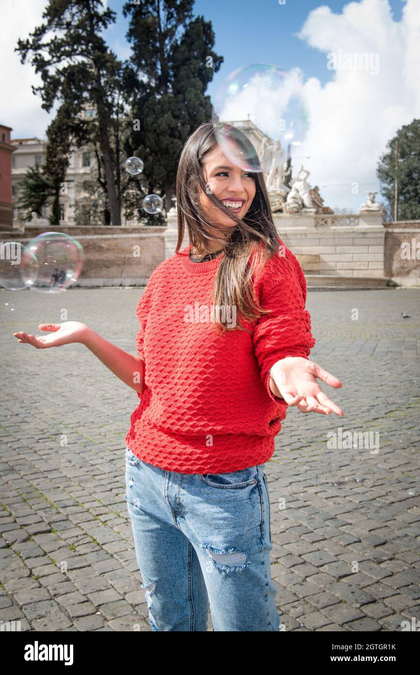 Cheerful Young Woman Standing Amidst Bubbles In City Stock Photo