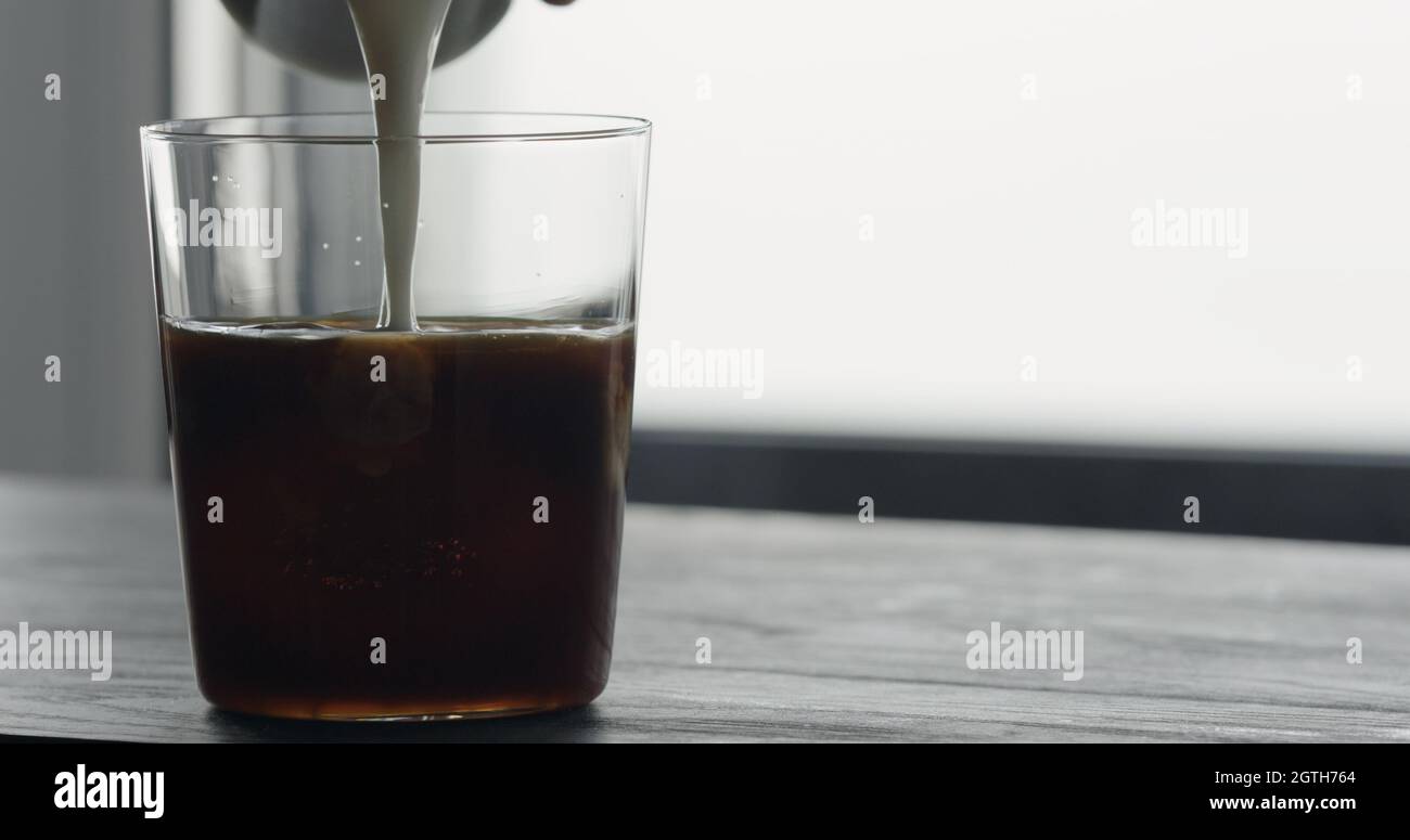pour milk into ice coffee on black wood table, wide photo Stock Photo