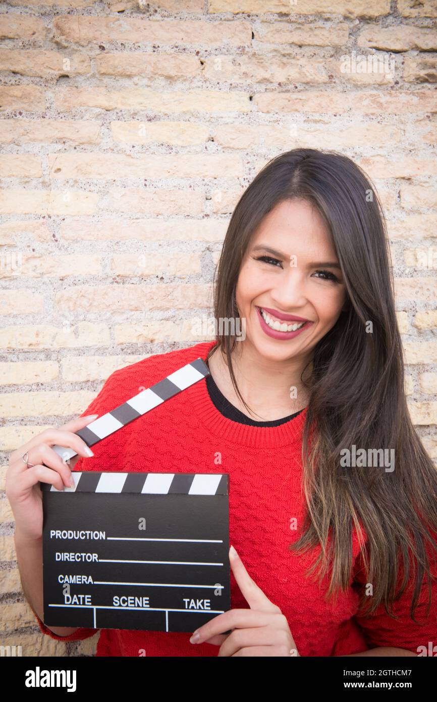Portrait Of Cheerful Young Woman Holding Film Slate By Brick Wall Stock Photo