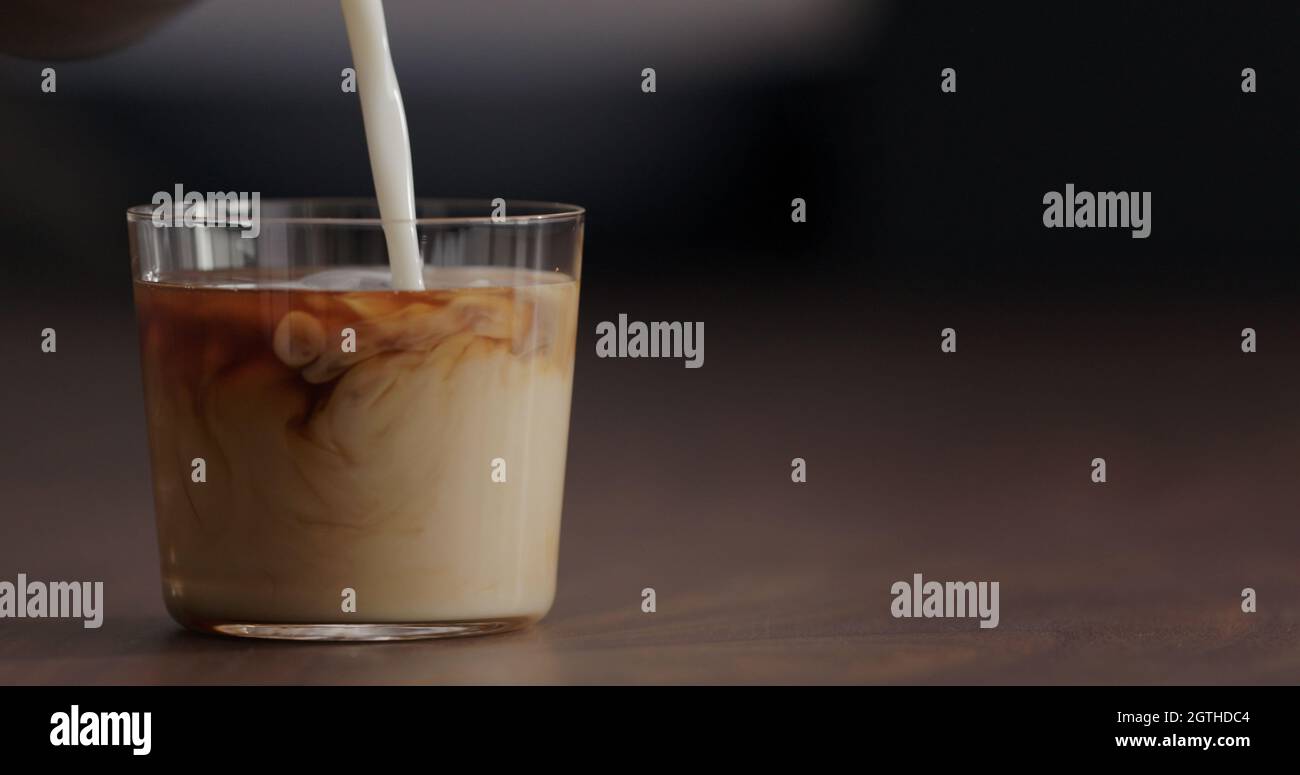 pour milk into ice coffee on black walnut table, wide photo Stock Photo