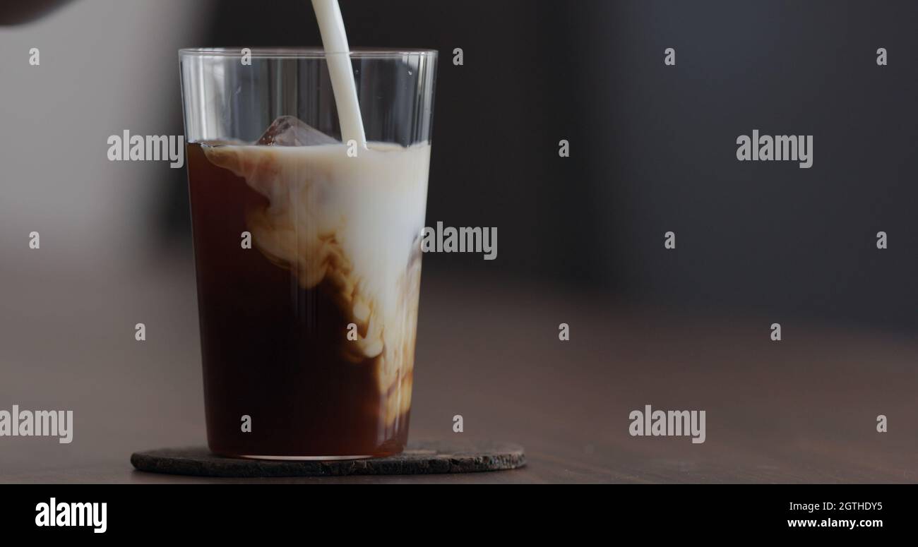 pour milk into ice coffee on black walnut table, wide photo Stock Photo