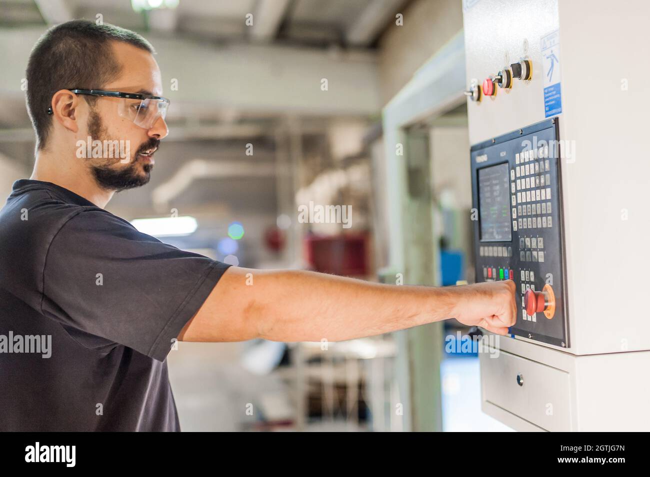 Close-up detail view of professional worker technician machinist pressing emergency stop button on control panel in factory production workplace. Indu Stock Photo