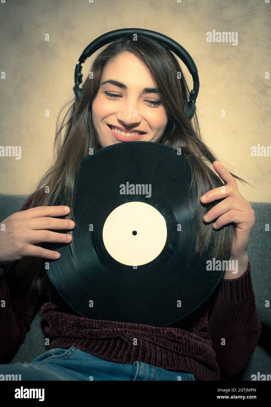 Woman Wearing Headphones While Holding Record By Wall Stock Photo