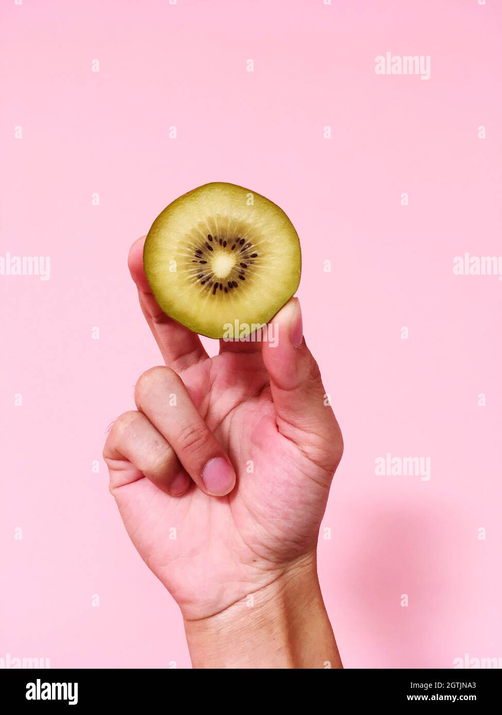 Cropped Hand Holding Kiwi Slice Against Pink Background Stock Photo