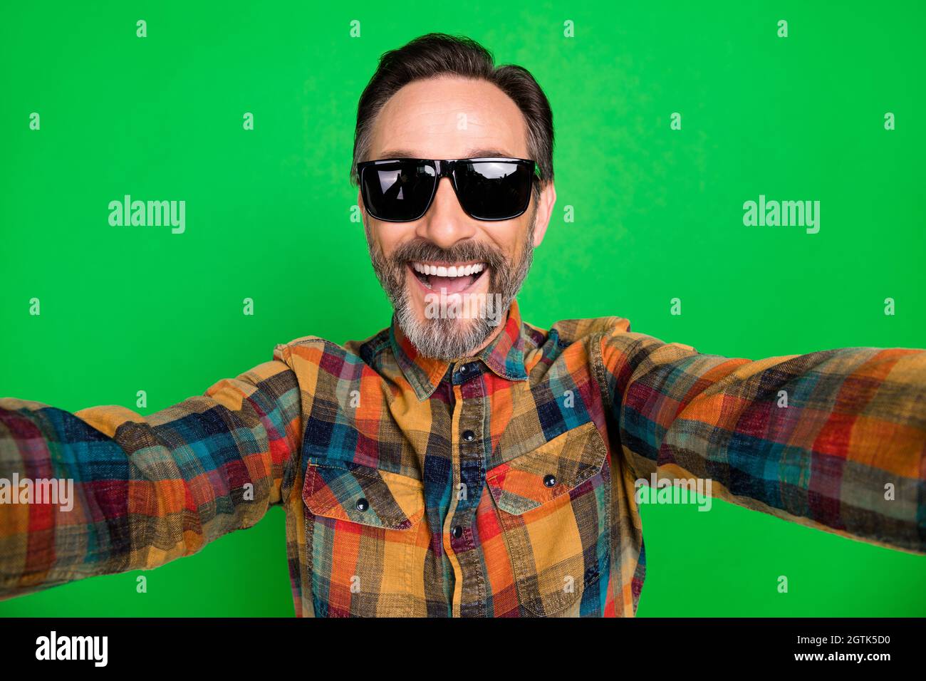 Self-portrait of attractive cheerful man wearing specs having fun isolated over bright green color background Stock Photo