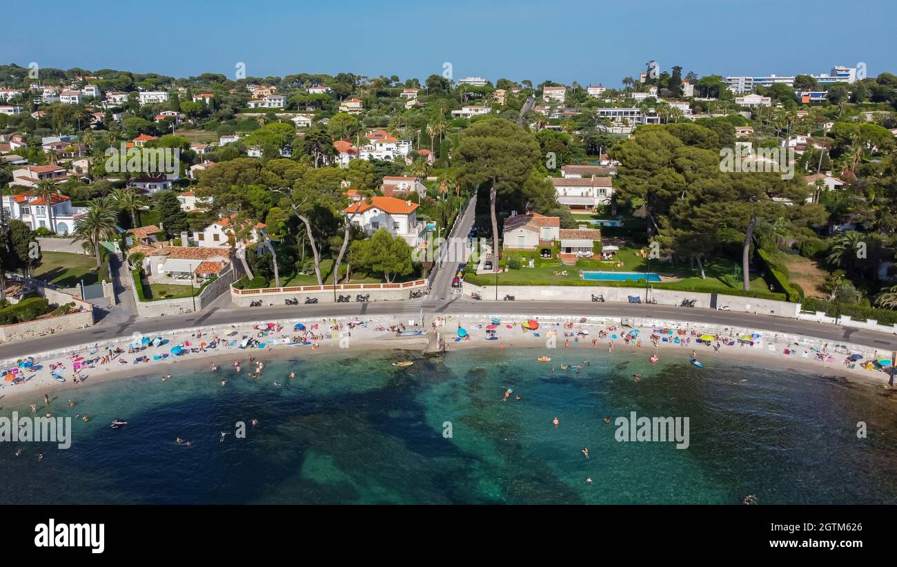 Aerial view of expensive estates behind Ondes Beach on the Cap d'Antibes in the French Riviera - Tourists sunbathing by the Mediterranean Sea in the S Stock Photo