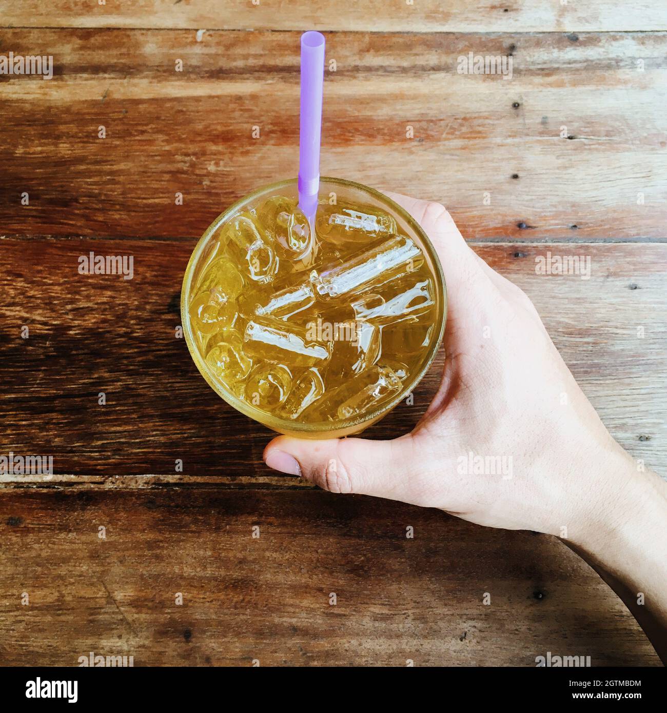 Cropped Hand Of Person Holding Cold Drink On Wooden Table Stock Photo
