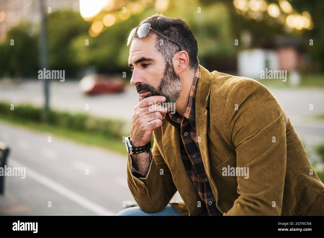 Worried businessman with a beard thinking while sitting on a bench in ...