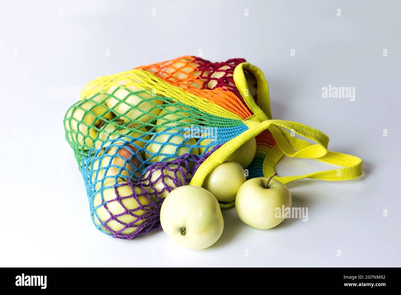 Reusable cotton string bag for shopping with green apples, multicolored rainbow LGBT trendy colors. It lies on a light table. The concept of zero wast Stock Photo