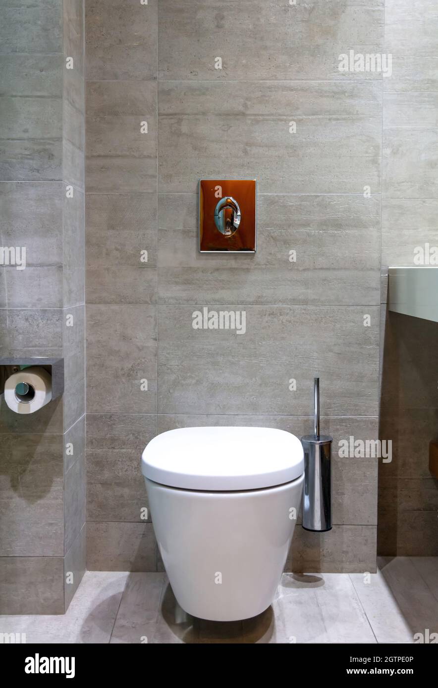 Modern toilet interior design, hanging toilet bowl, brush and flush button. Luxury lavatory accessories on marble tiled walls and floor light gray col Stock Photo