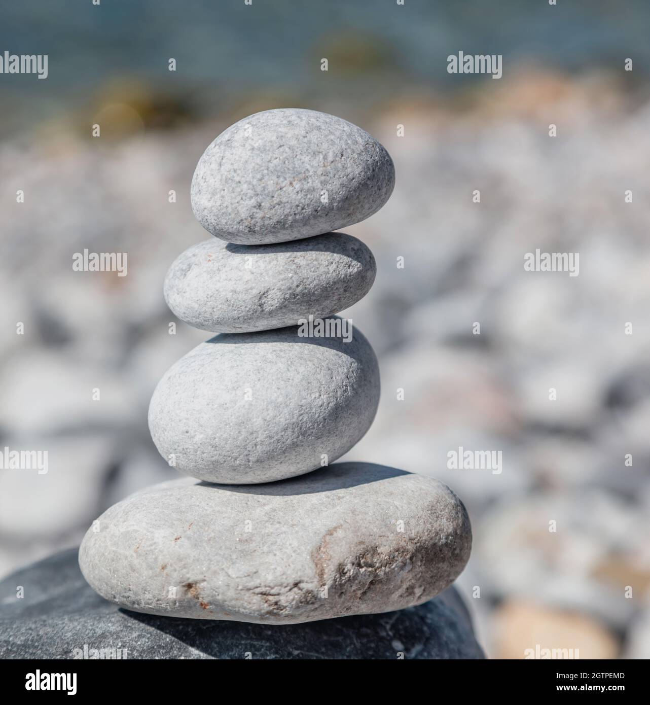 Feng shui, harmony and peace concept. Balance, zen stones, smooth rock tower stacked on pebble beach, blue sea background, sunny day. Stock Photo