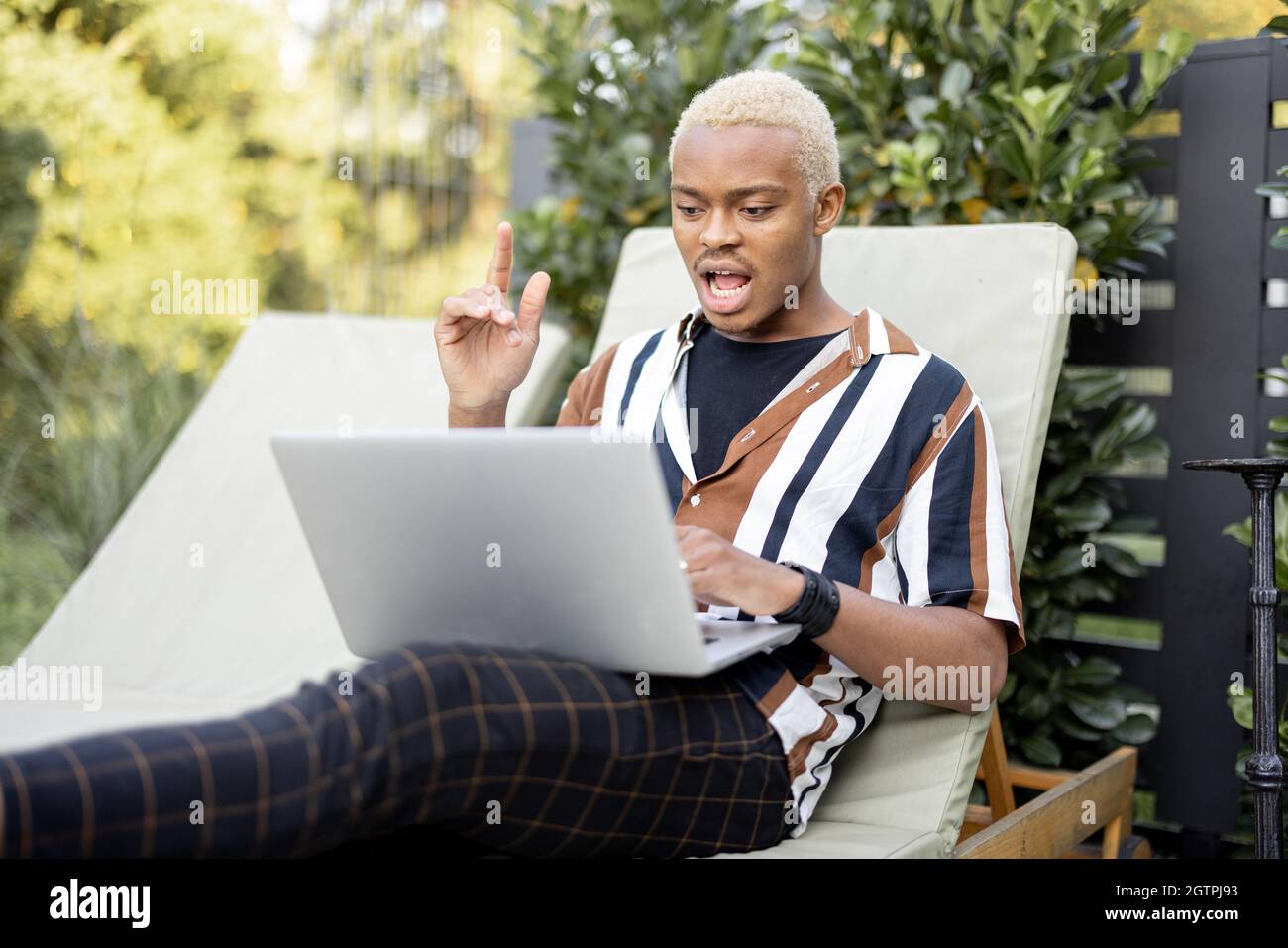 Black man using laptop on lounger at house garden Stock Photo