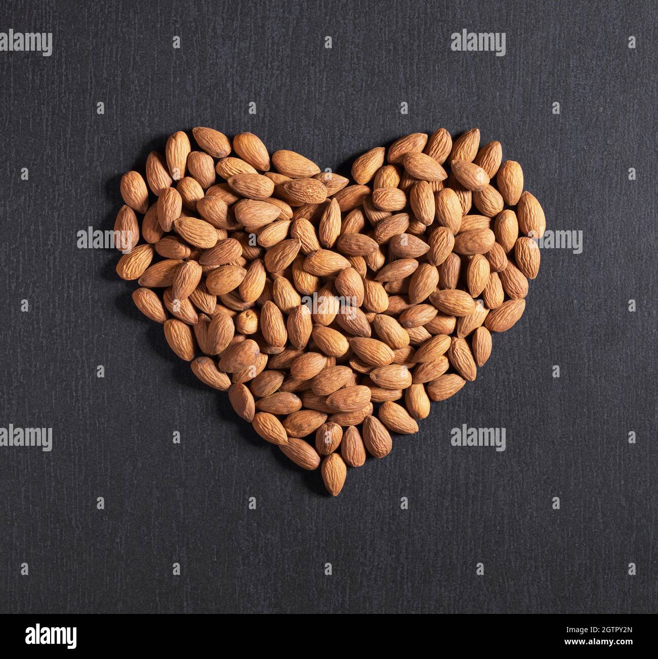 Almond nuts in the shape of heart on a black stone background, top view ...