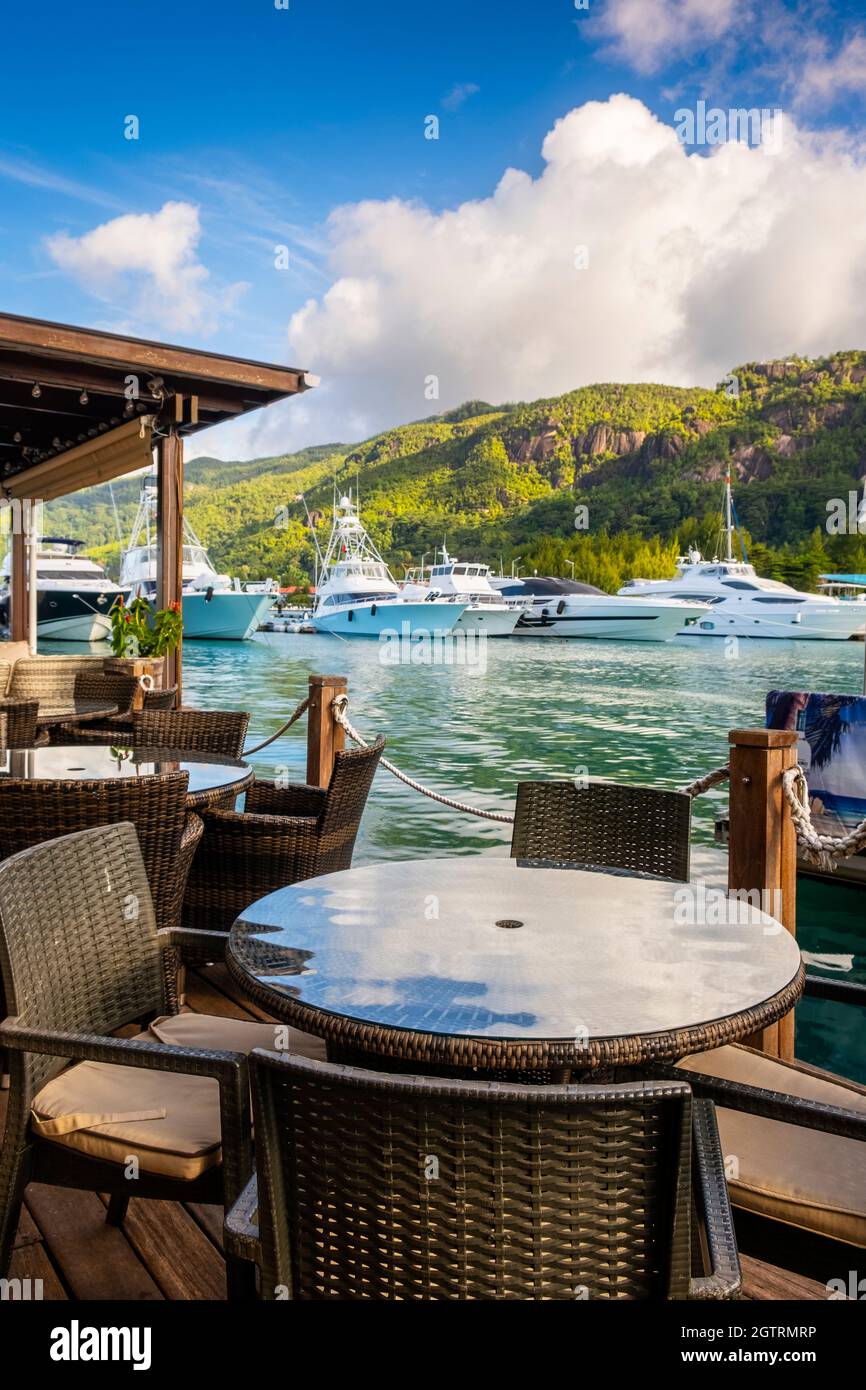 Chairs And Tables At Restaurant By Sea By Eden Island, Seychelles, Against Sky Stock Photo
