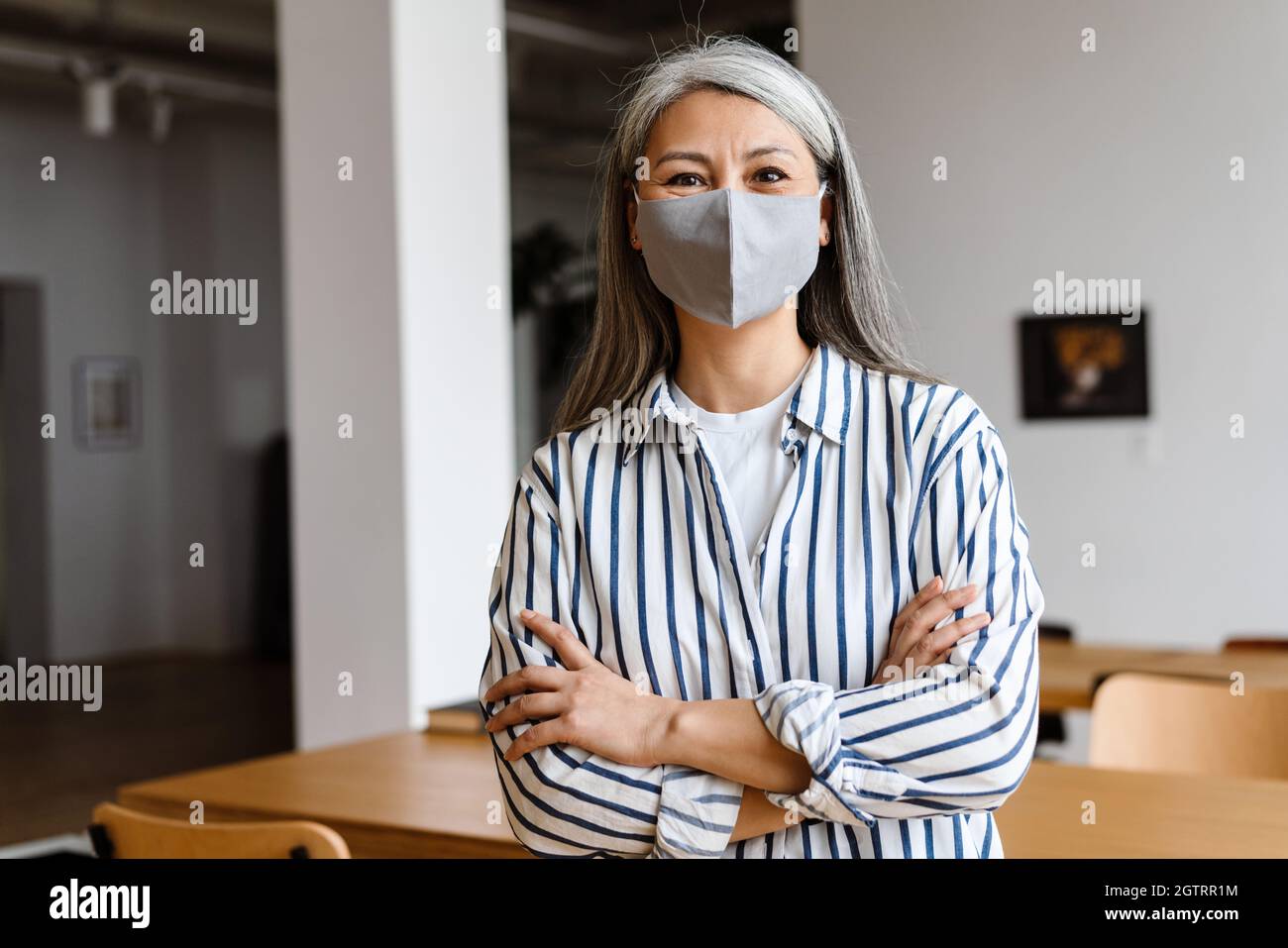 Confident woman office worker in face mask standing arms folded Stock Photo