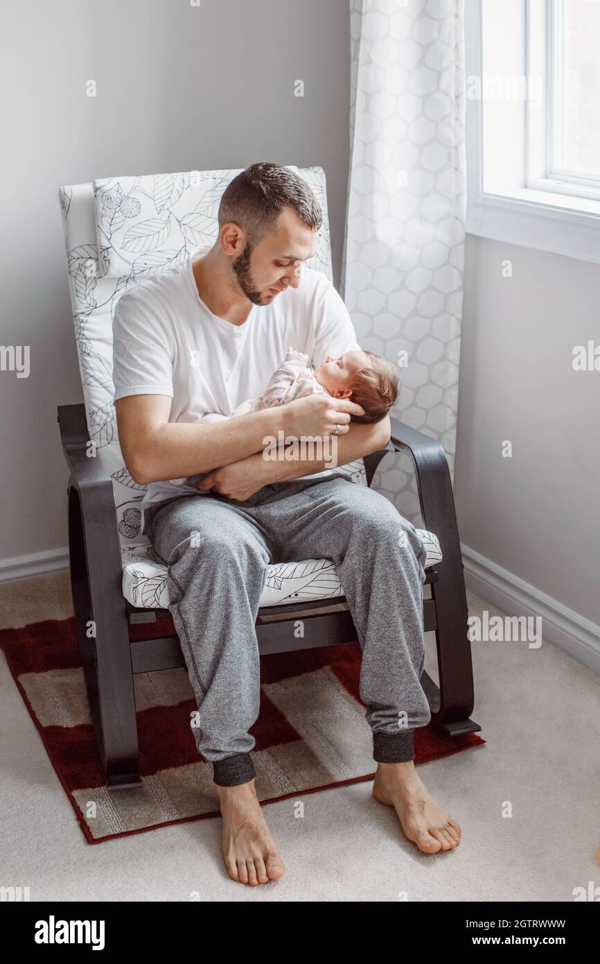Caucasian father sitting in armchair with newborn baby girl. Parent