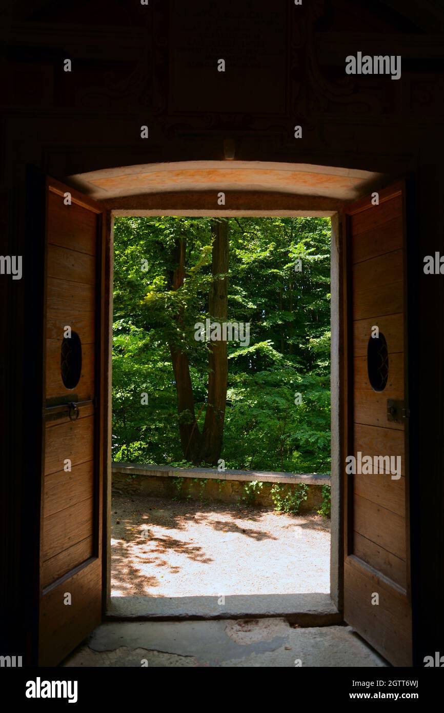 Vertical shot of the double wooden open door leading to the beautiful area with green trees Stock Photo