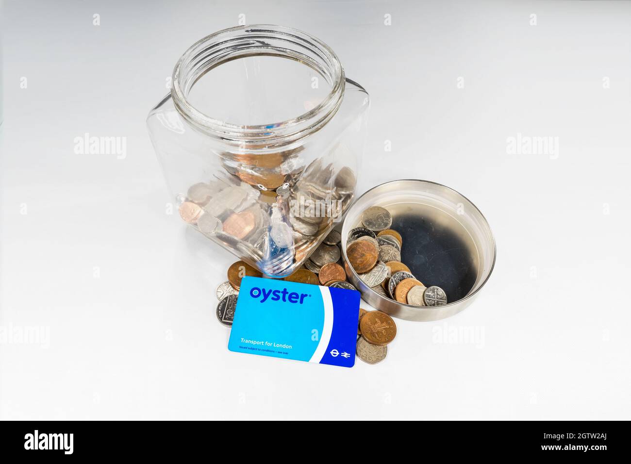 Oyster prepaid travel card in front of a glass jar of loose change on a white background. Stock Photo