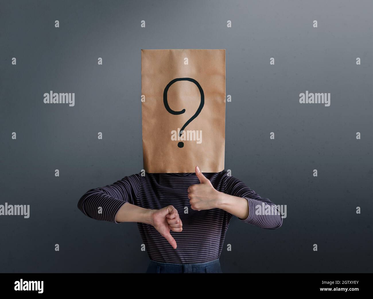 Person Wearing Paper Bag With Question Mark While Gesturing Against Gray Background Stock Photo