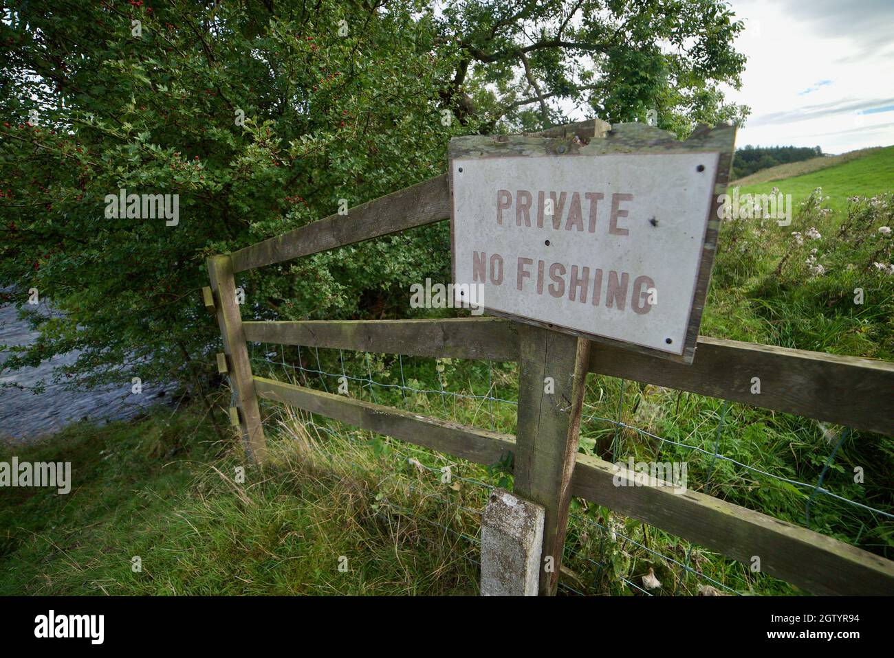 PRIVATE- NO FISHING sign on a fence next to a river/stream in Northumberland, UK. A wooden fence with a sign post saying 'Private No Fishing'. Stock Photo